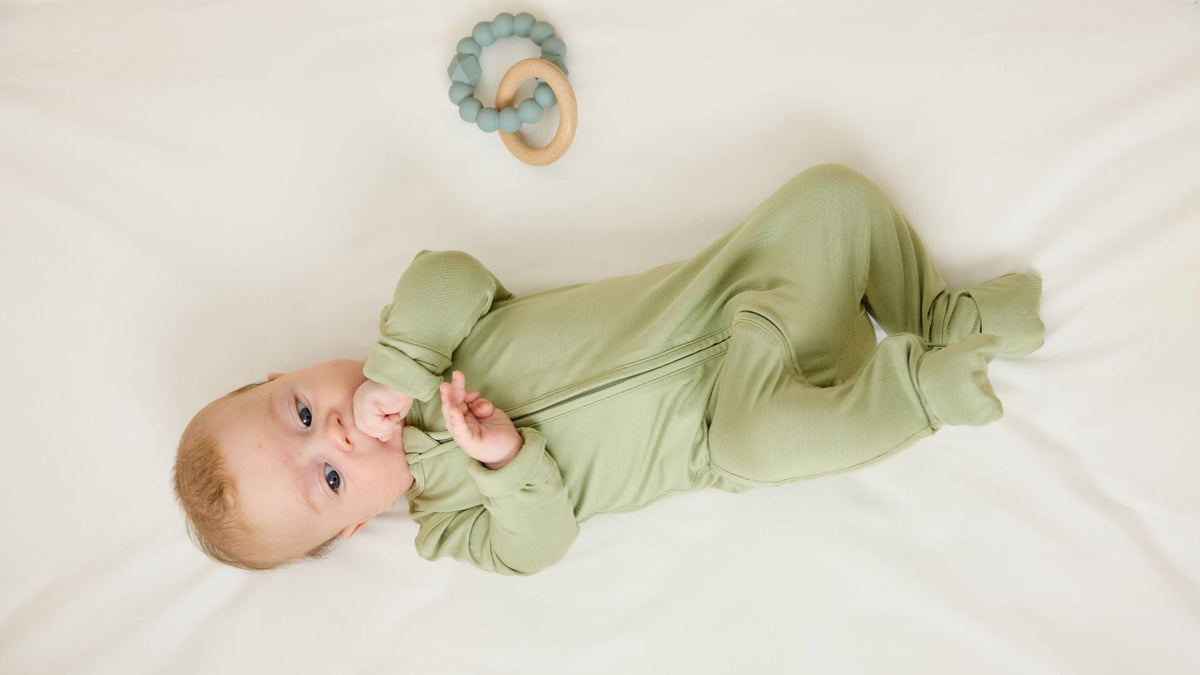 Baby wearing a soft green zip romper lying beside a wooden teething toy.
